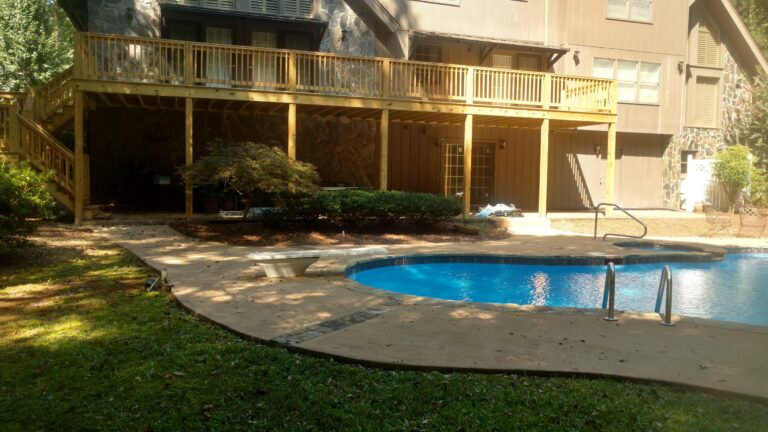 Backyard view of newly built elevated wooden deck overlooking a swimming pool, completed by Thaxton Construction in Griffin, GA.