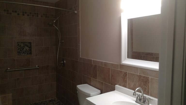 Custom walk-in shower with stone tile walls, built-in niche, handheld showerhead, and modern vanity installed by Thaxton Construction in Griffin, GA