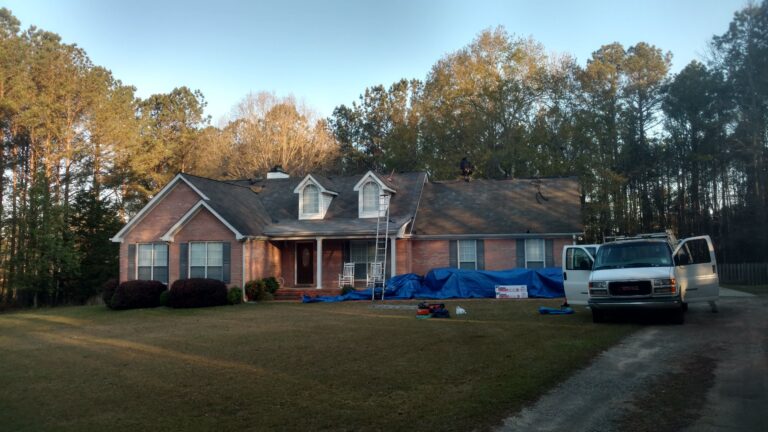 Residential roof replacement project in progress on a brick home in Georgia, with workers, tarps, and roofing materials on site