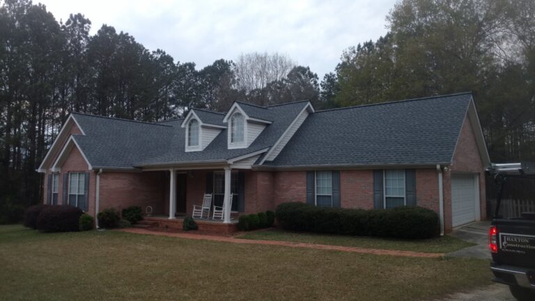 A brick house with a dark gray Asphalt Shingles roof, multiple dormer windows, and a covered front porch with white rocking chairs.