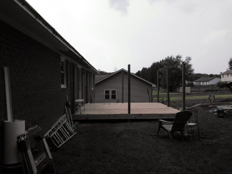 A residential backyard with a newly built wooden deck and a house in the background, featuring a visible roof that may require roofing repair services.