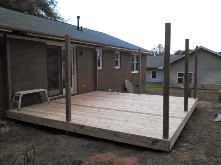 A newly constructed wooden deck extends from a brick residential home with a wooden roof getting installed