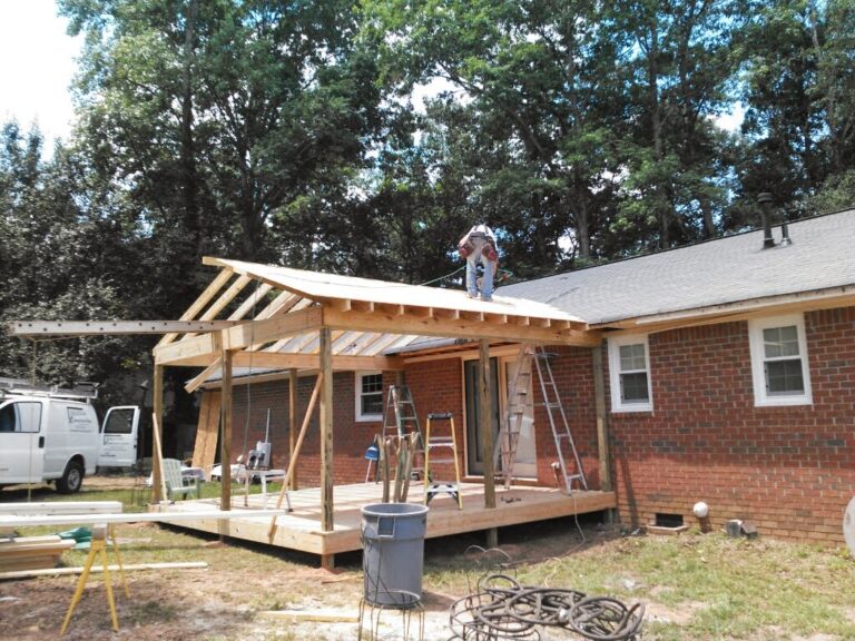 A newly constructed wooden deck extends from a brick residential home with a wooden roof getting installed half way