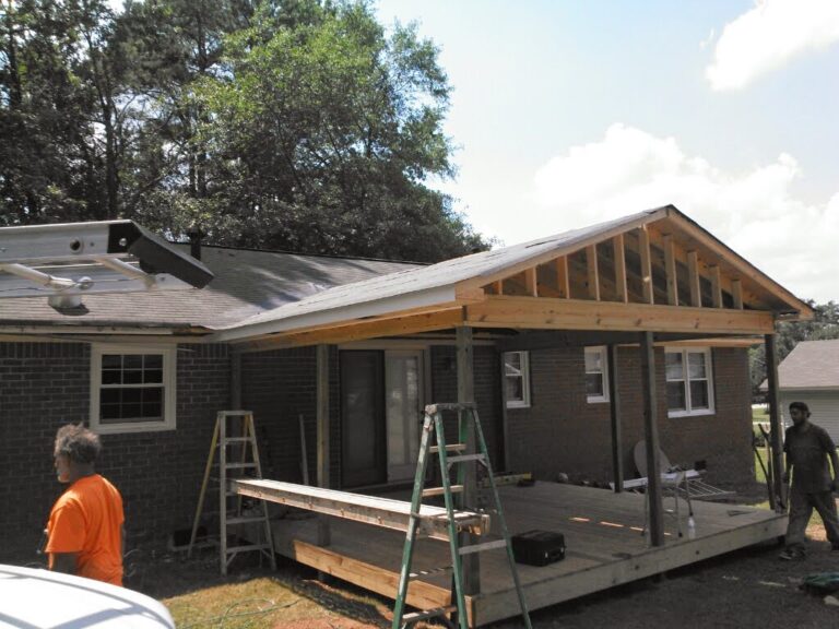 Newly constructed wooden deck extends from a brick residential home with a wooden roof getting installed making it a lobby